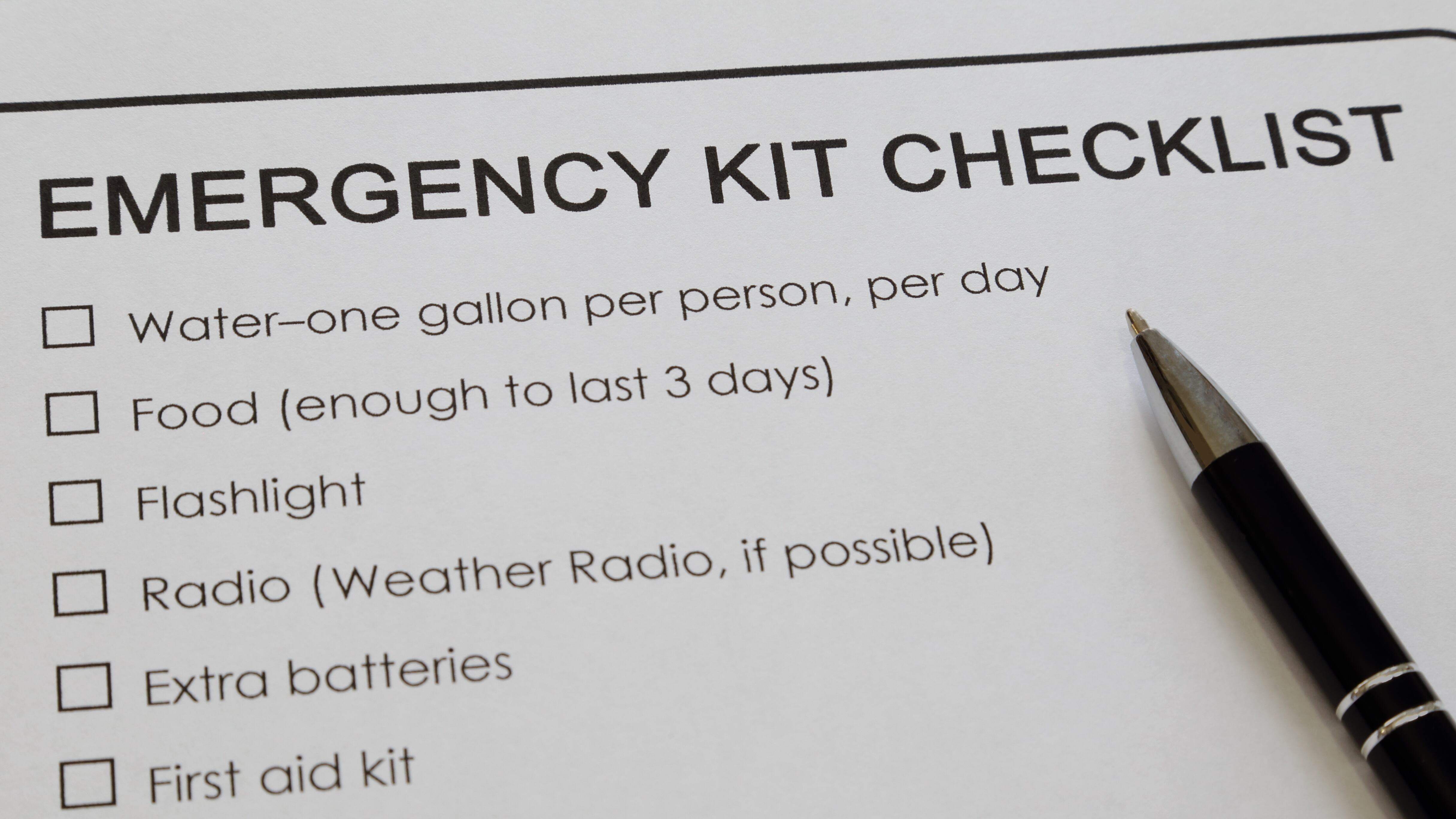 An emergency kit checklist printed on white paper and ink pen are shown close.
