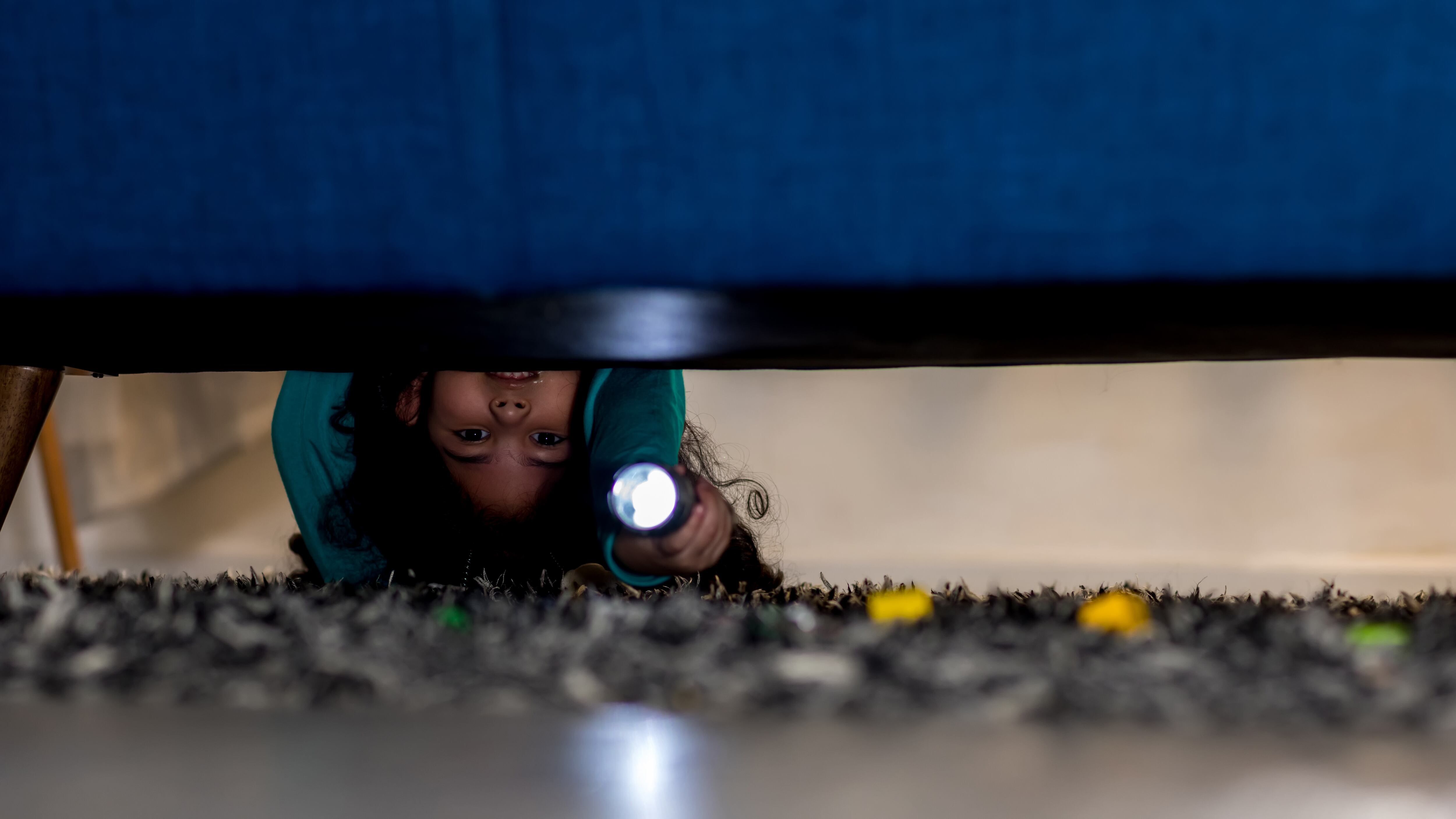 A child looking under a bed with a flashlight.